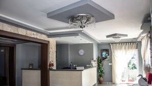 A modern reception area with a reception desk, a clock, and a chandelier. - Ilios Hotel (Kassandra)