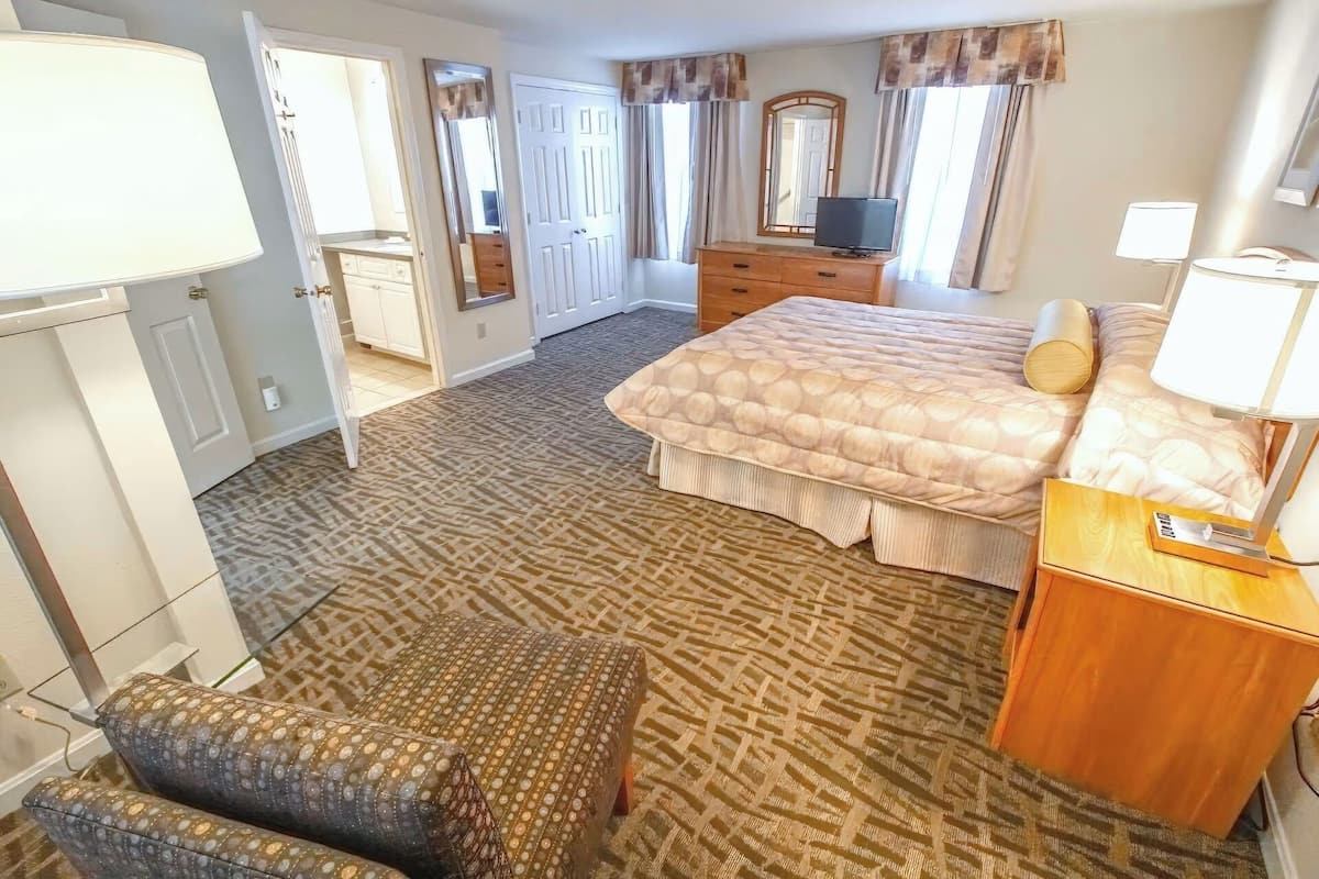 A hotel room with a bed, a desk, a chair, a dresser, and a TV.