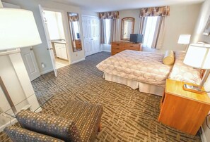 A hotel room with a bed, a desk, a chair, a dresser, and a TV.