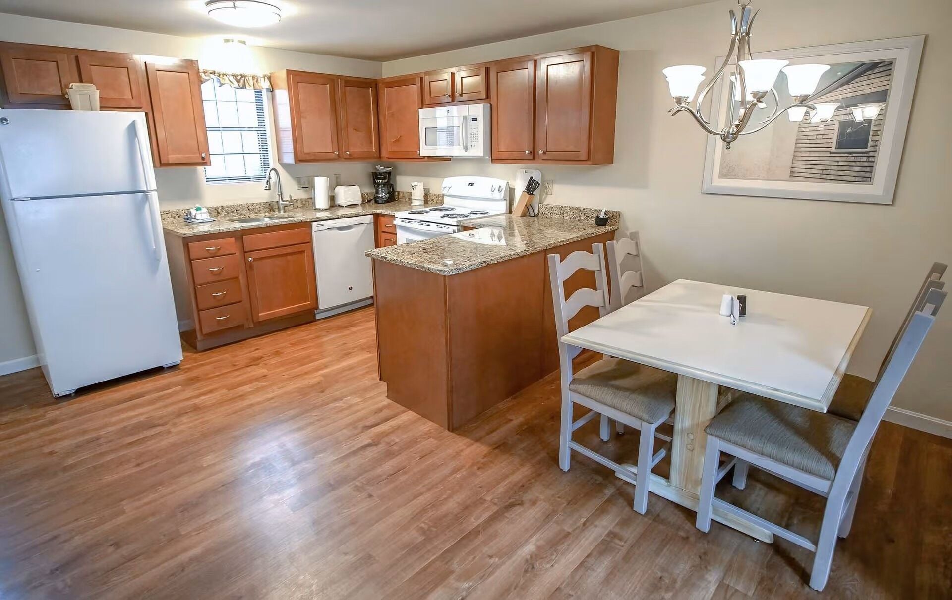A kitchen with wooden cabinets, a white refrigerator, a microwave, a stove, and a dining area with a white table and chairs.