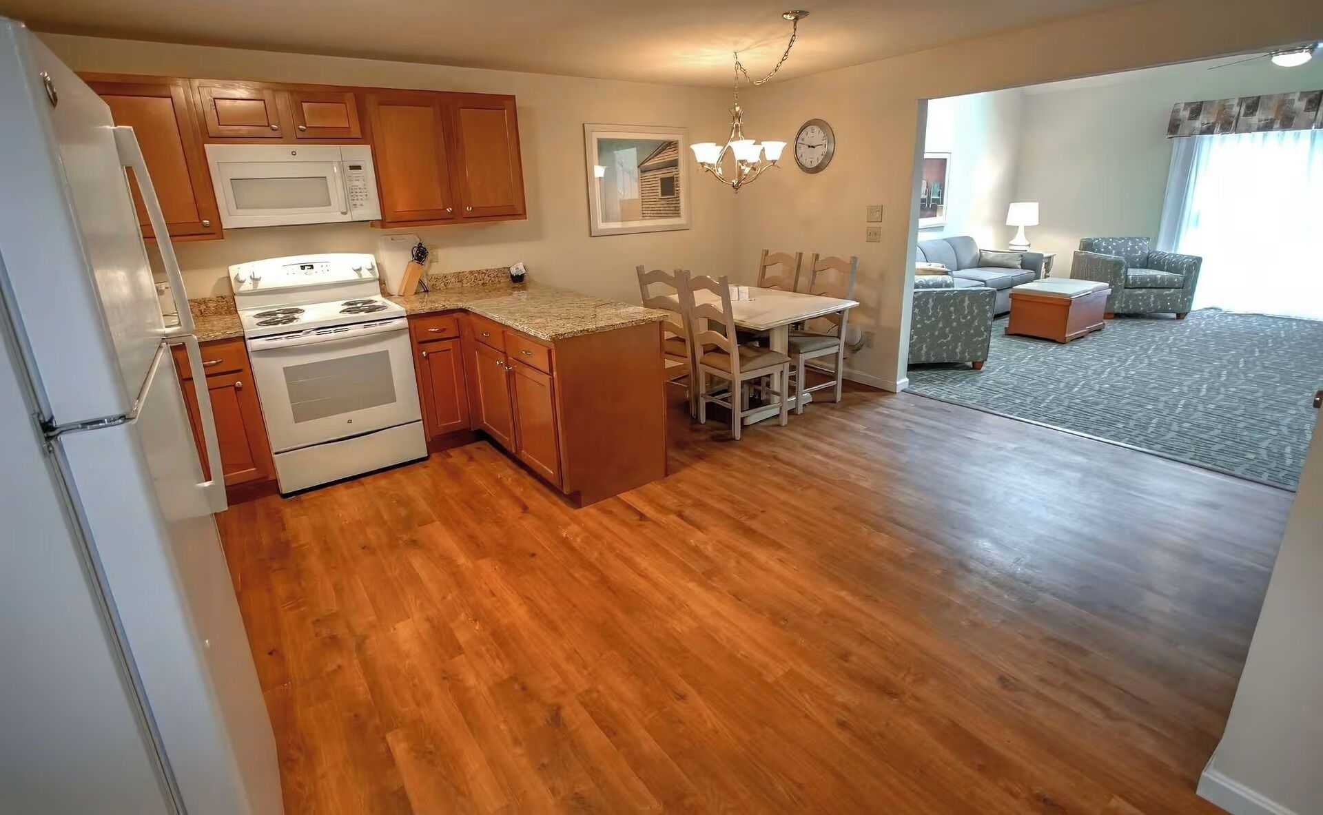 A kitchen with wooden cabinets, a microwave, stove, and a dining area with a table and chairs.