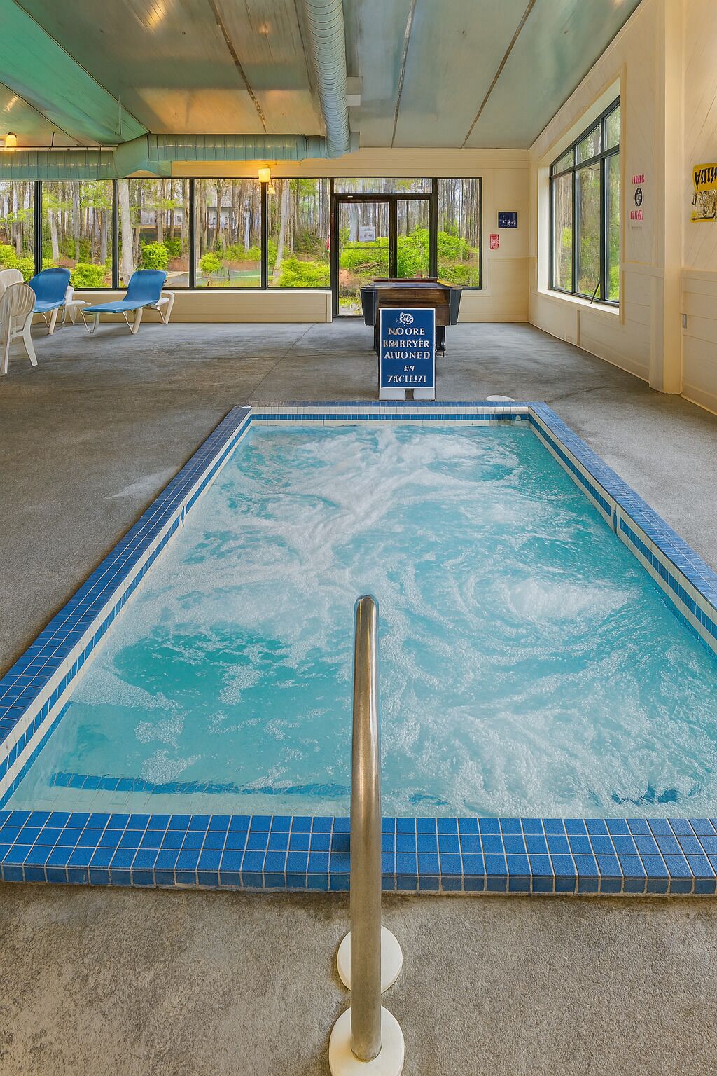 Una piscina interior con borde de azulejos azules, una escalera metálica y un cartel que indica que la piscina está fuera de servicio.