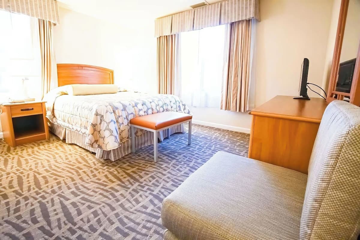 A hotel room with a bed, a bench, a desk, and a chair.
