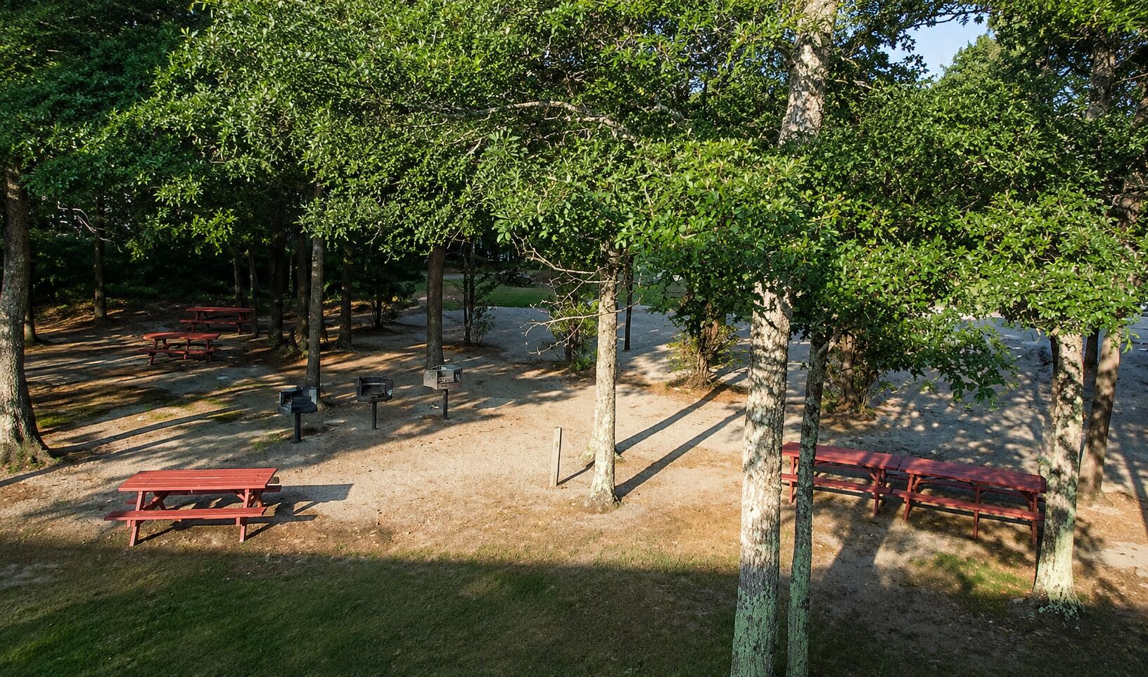 A park with picnic tables and benches, surrounded by trees.
