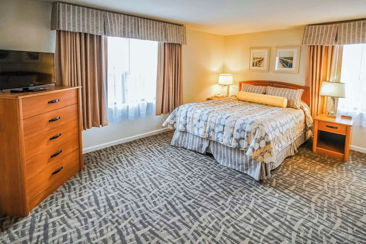 A hotel room with a bed, a dresser, a TV, and a window with curtains.