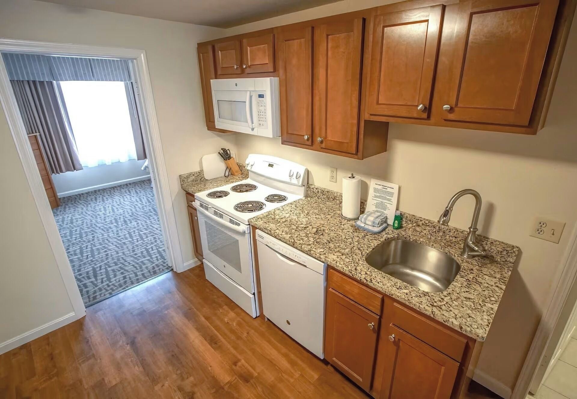 A compact kitchen with wooden cabinets, a microwave, a stove, and a sink.