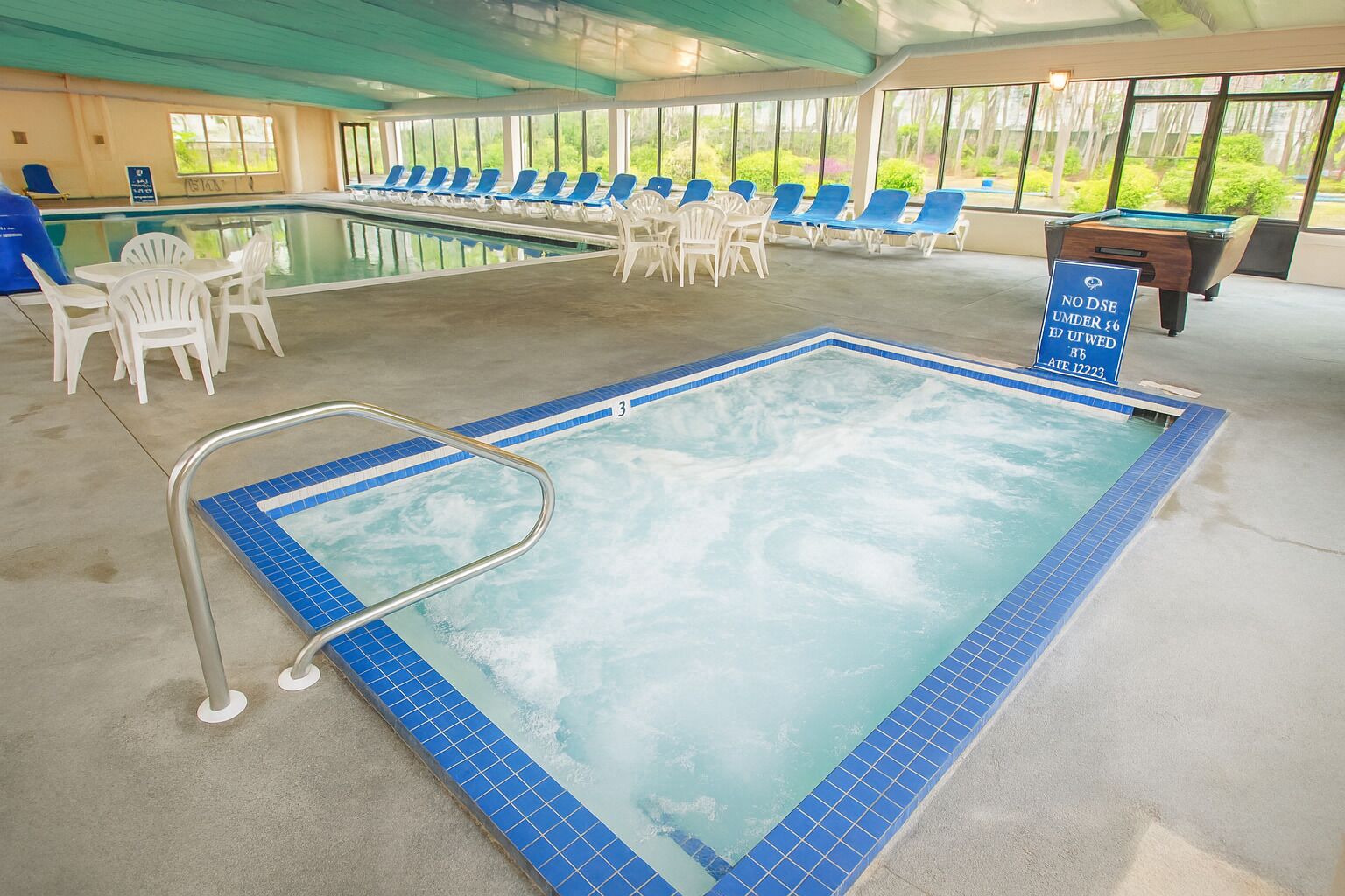 En swimmingpool med blå fliskanter, en badestige og liggestole.