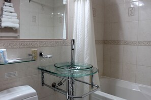 A bathroom with a glass sink, a toilet, and a bathtub.