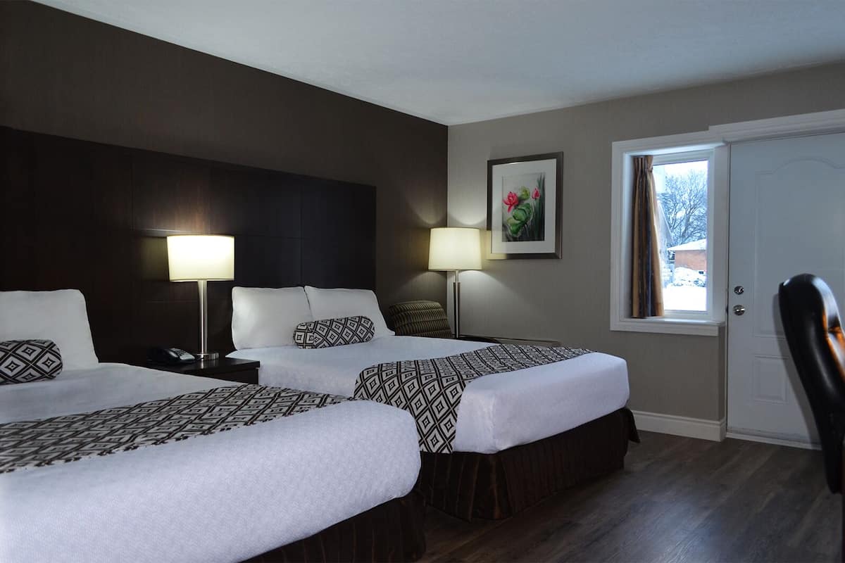 A hotel room with two beds, a desk, a chair, a window with a view, and a door.