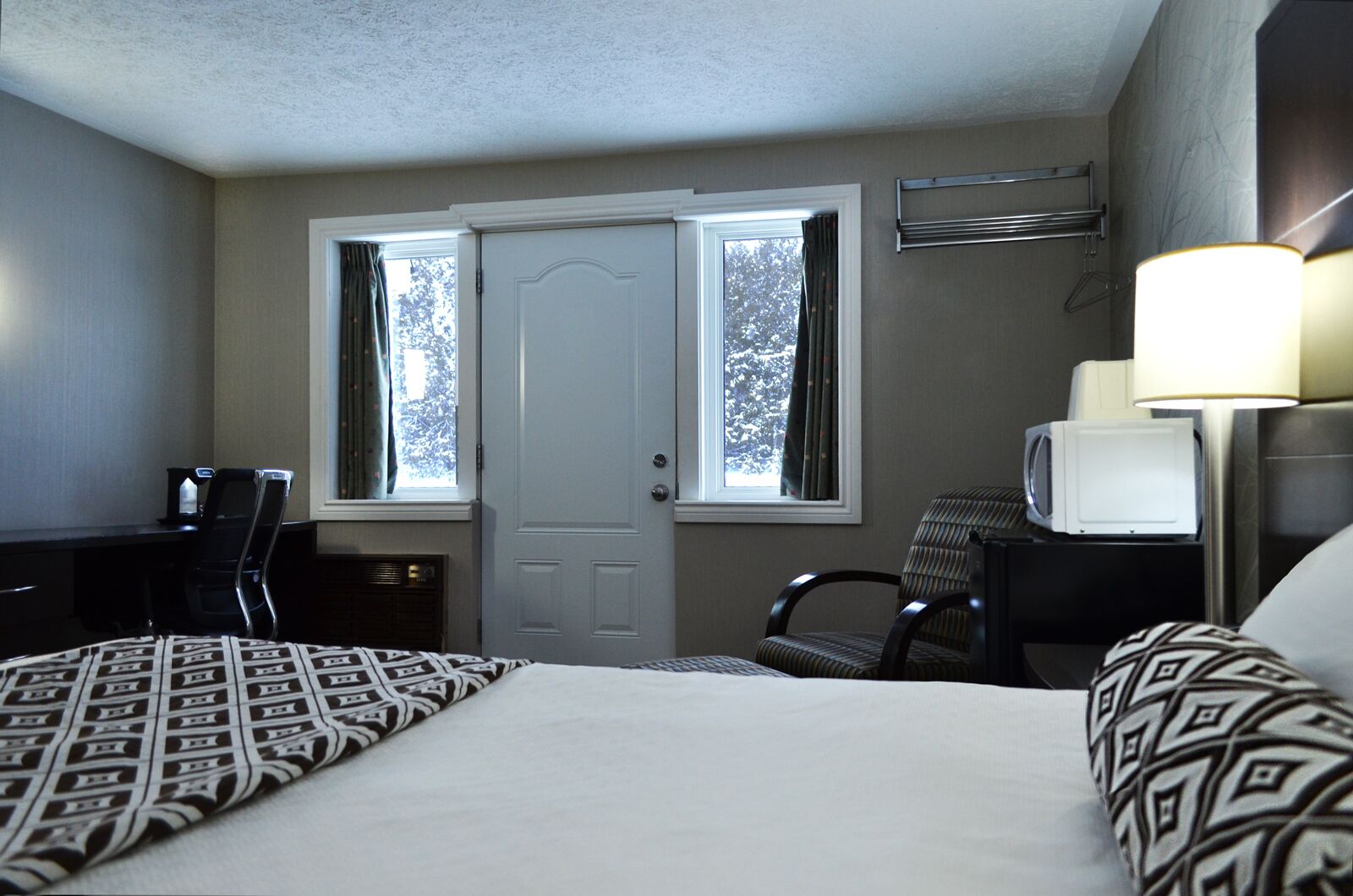 Habitación de hotel con cama, dos sillas, escritorio, televisor y ventana con cortinas.