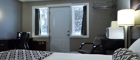Habitación de hotel con cama, dos sillas, escritorio, televisor y ventana con cortinas.