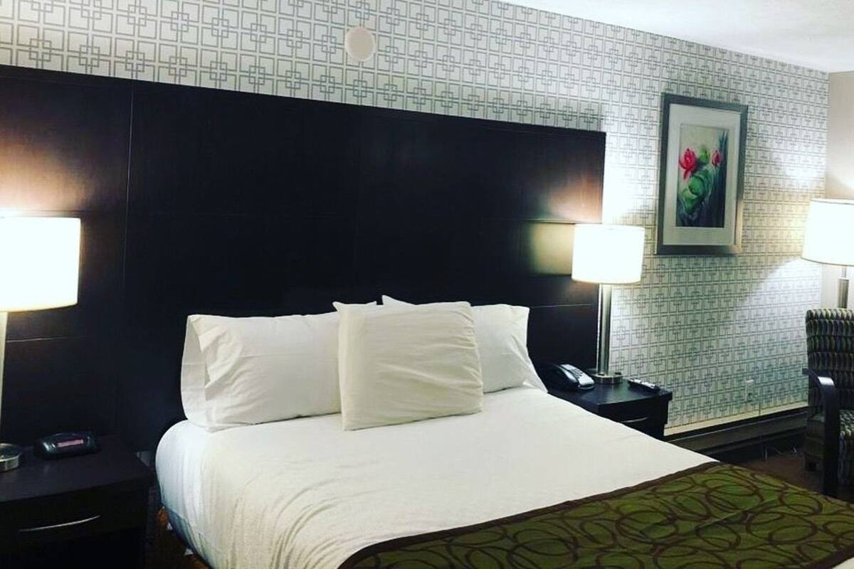 A hotel room with a large bed, two bedside tables, a chair, and a painting on the wall.
