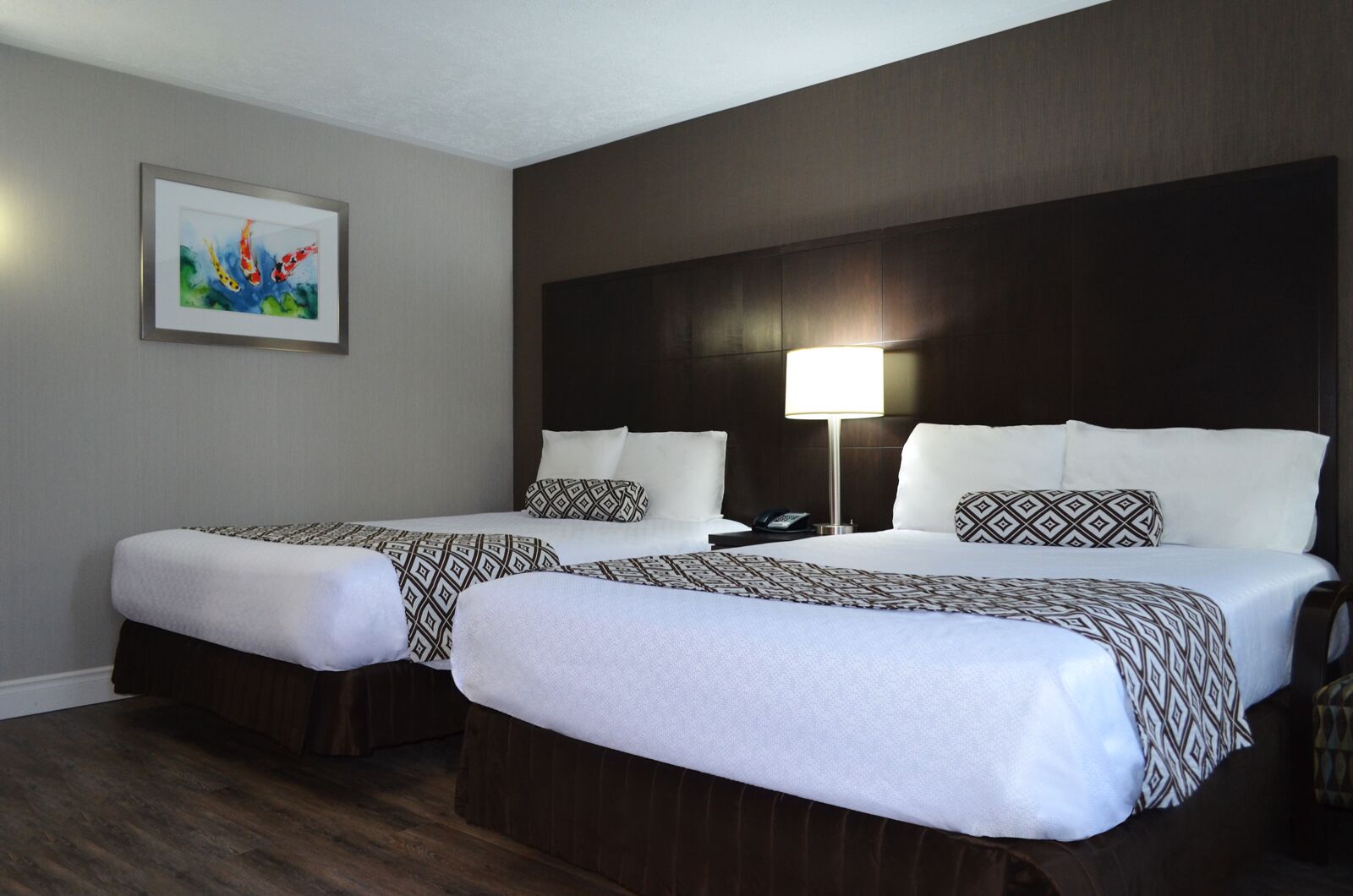 A hotel room with two beds, a nightstand with a lamp, and a painting on the wall.