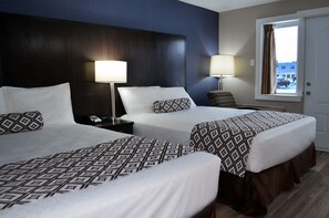 A hotel room with two beds, each with patterned bedding, a dark headboard, bedside lamps, and a window with curtains. - Travellers Inn Hanover (Hanover)