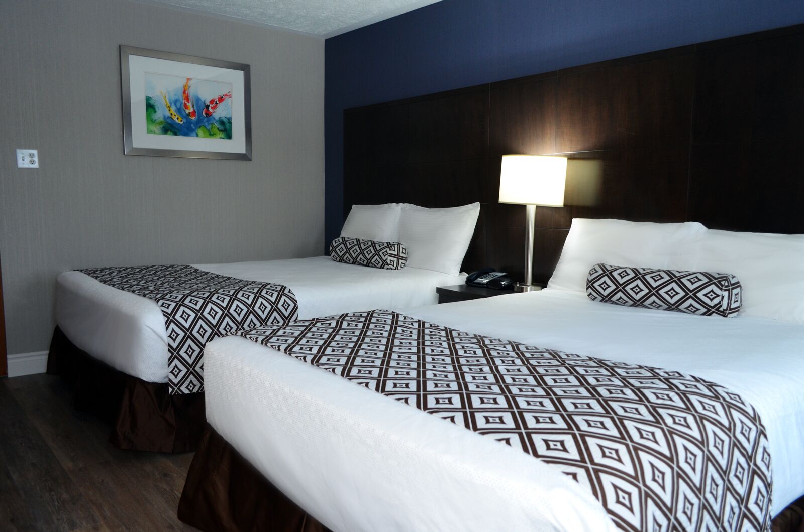 A hotel room with two beds, each with patterned bedding, a nightstand with a lamp, and a framed painting on the wall.