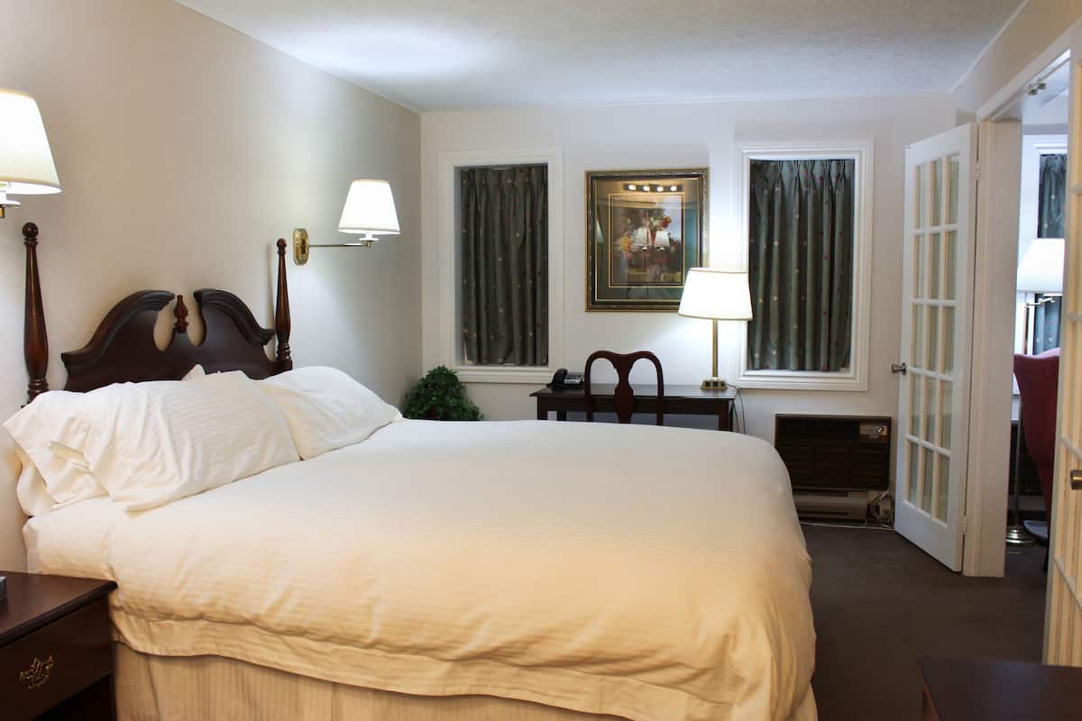 A neatly arranged hotel room with a large bed, bedside lamps, a small table, and a door leading to another room.