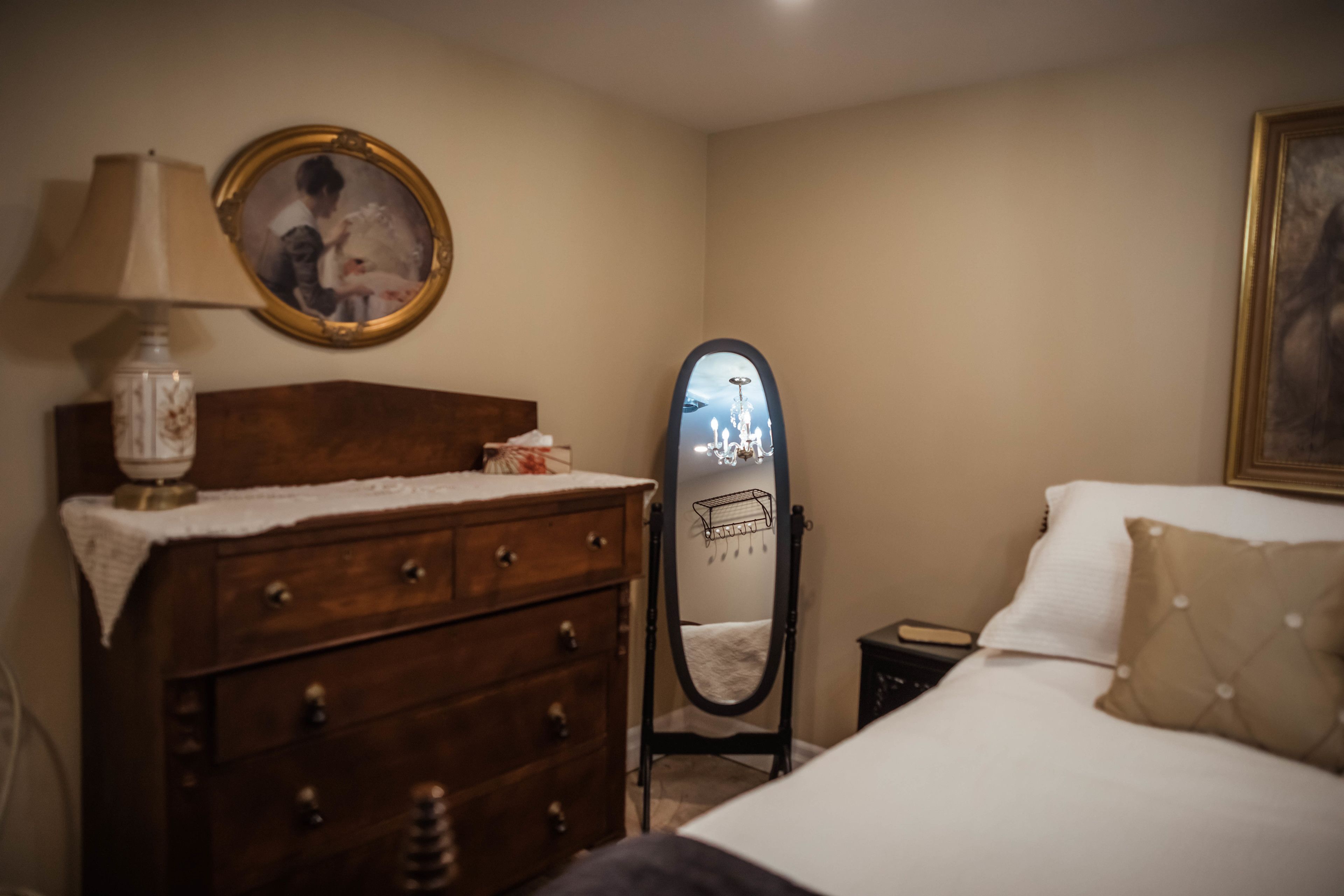 Un dormitorio con un aparador de madera, un espejo, una cama con edredón blanco y un cuadro enmarcado en la pared.