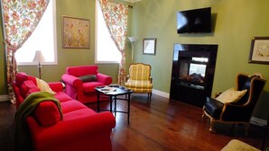 A living room with red sofas, a striped armchair, a fireplace, and a television on the wall. - The Chepstow Inn (Brockton)