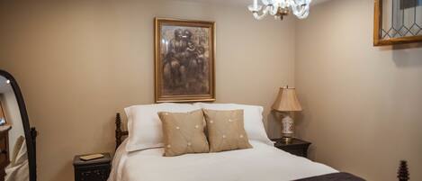 A neatly made bed with a headboard, a bedside lamp, and a framed artwork on the wall.
