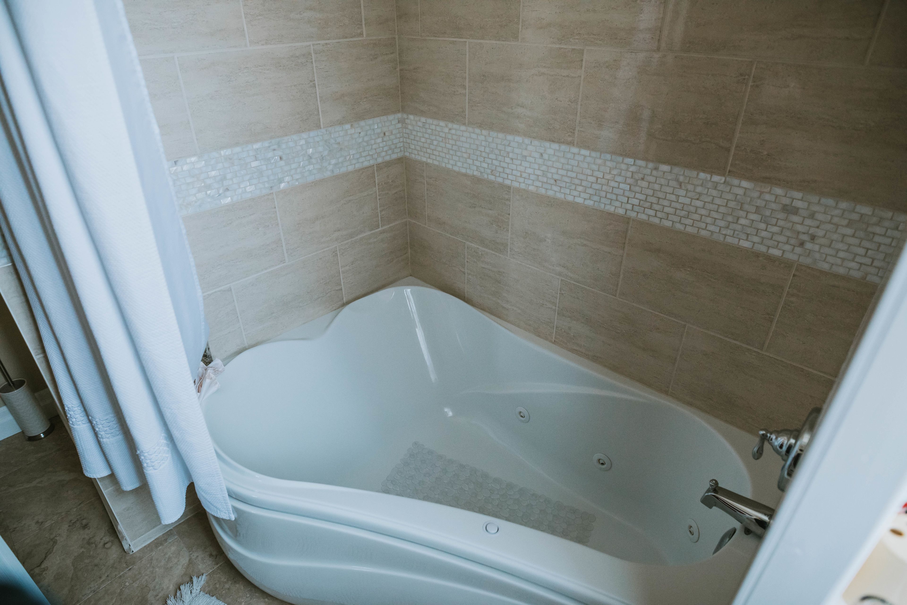 A bathroom with a bathtub, beige tiles, and a white tiled border.