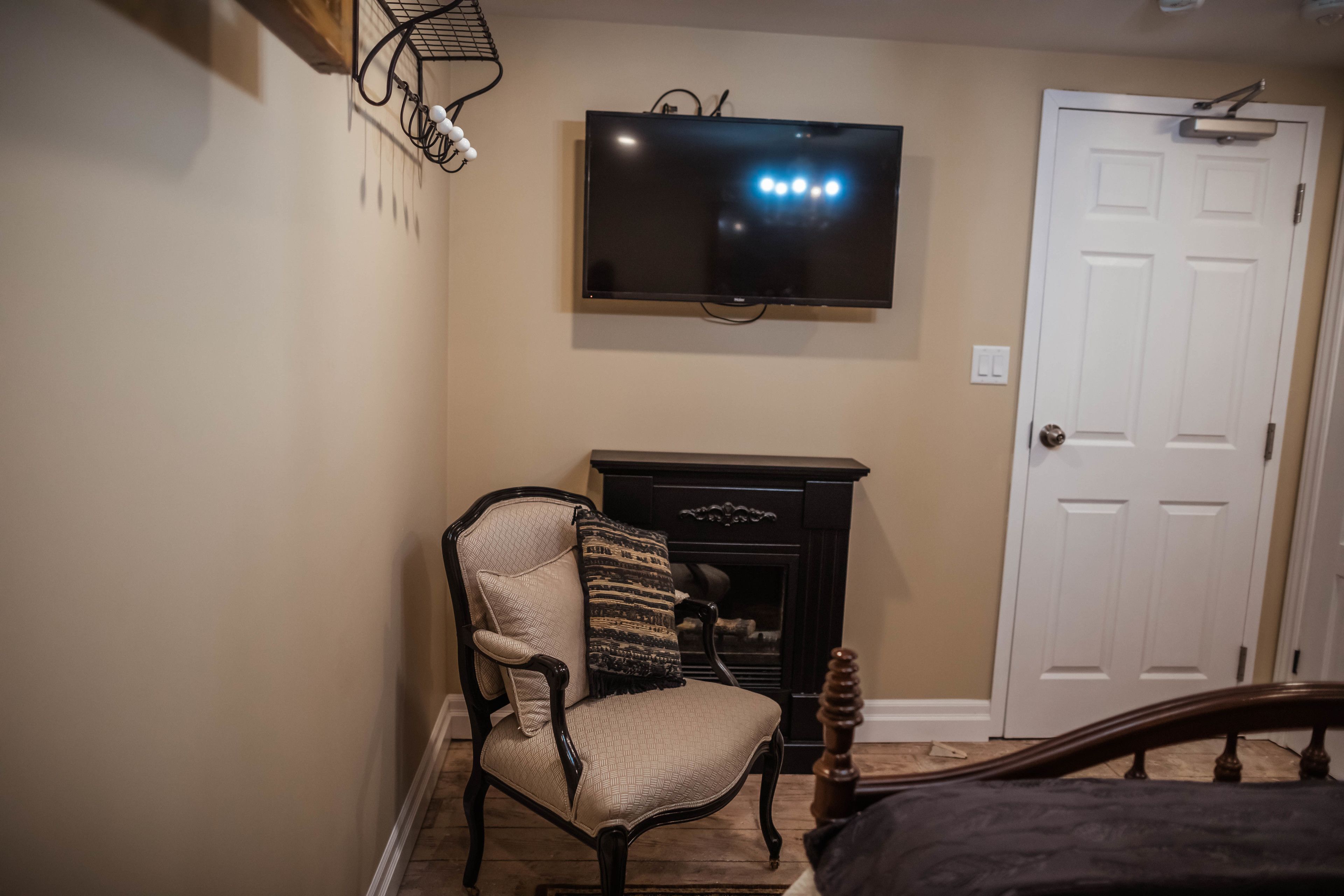 A room with a television mounted on the wall, a fireplace, a door, and a chair.