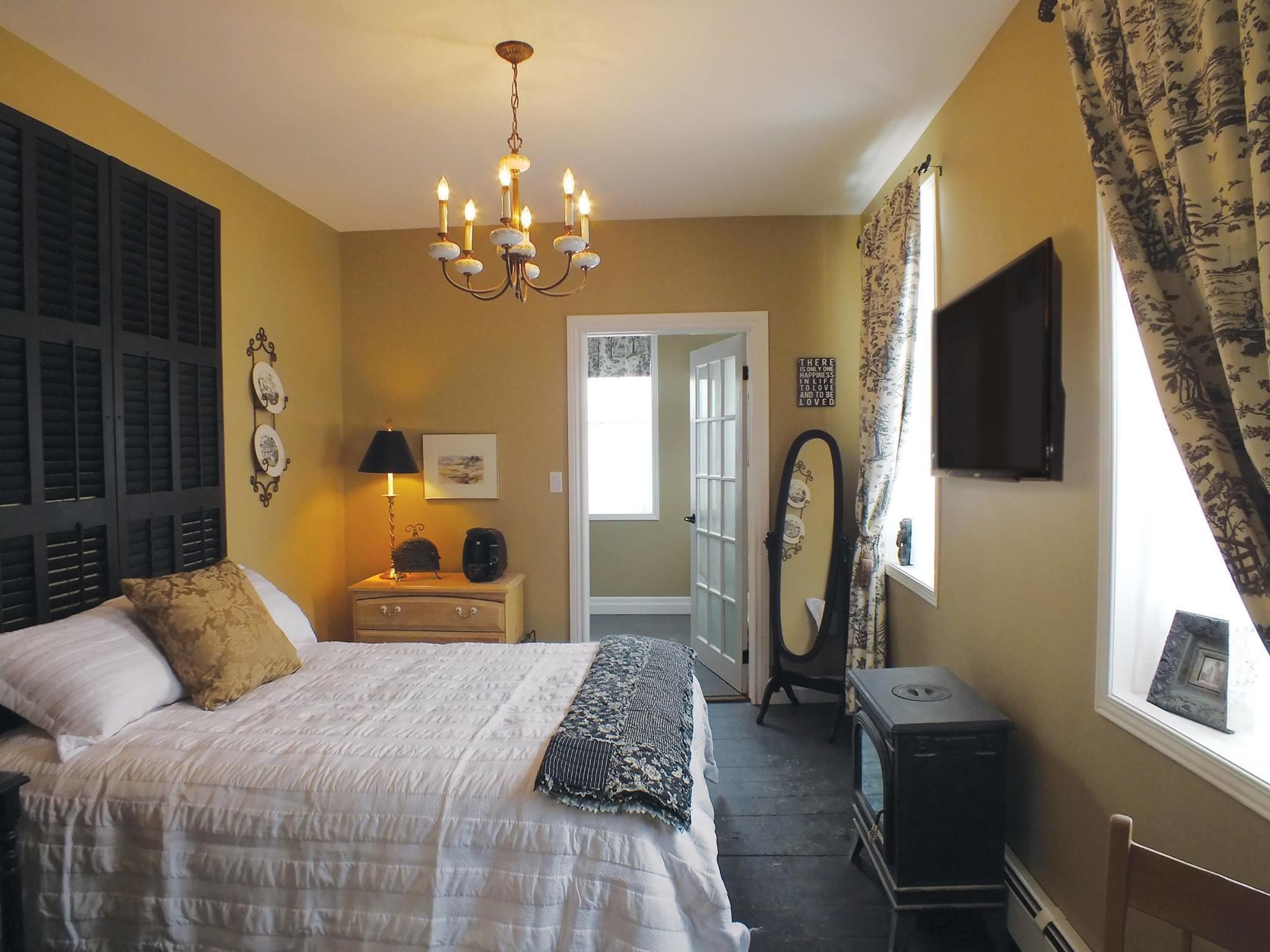 A bedroom with a bed, bedside table, lamp, dresser, mirror, and a television on the wall.