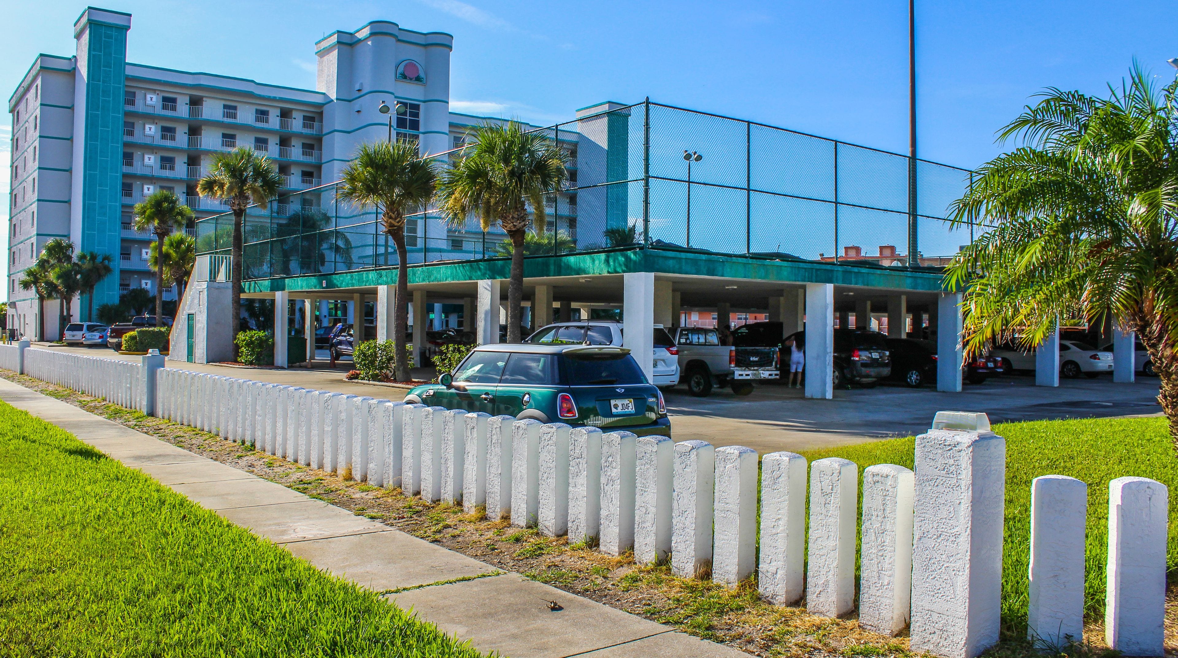 A hotel with a parking garage, a fenced parking area, and palm trees.