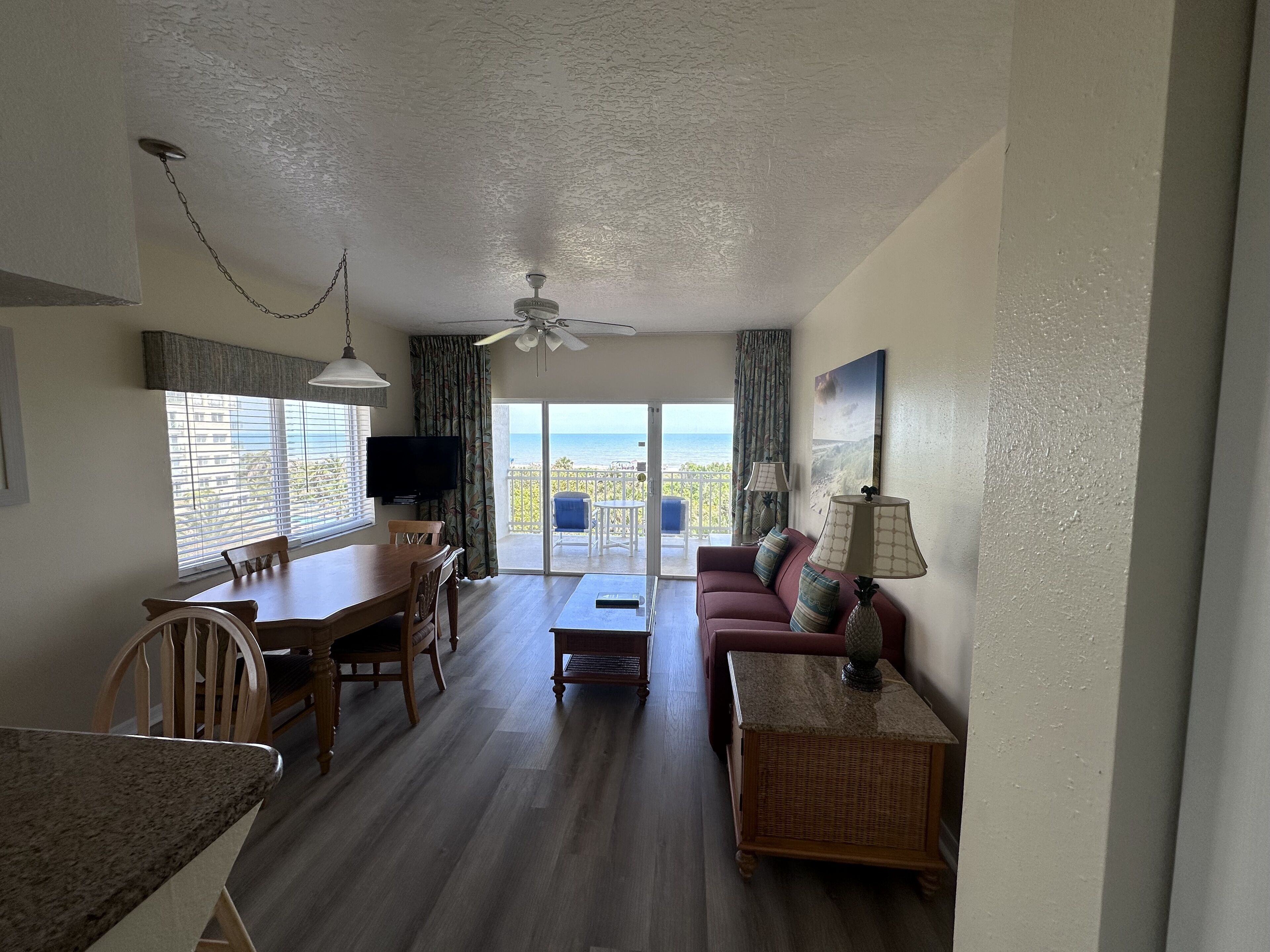 Un salon spacieux comprenant un coin repas, un ventilateur de plafond, un téléviseur et un balcon avec vue sur l’océan.