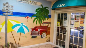 Un mural con temática playera que muestra un coche antiguo, palmeras y una sombrilla.