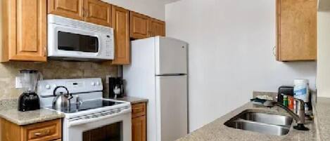 A kitchen with wooden cabinets, a white microwave, a white refrigerator, a stove, and a granite countertop.