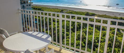 A balcony with a white table and chairs, overlooking a beach and ocean.