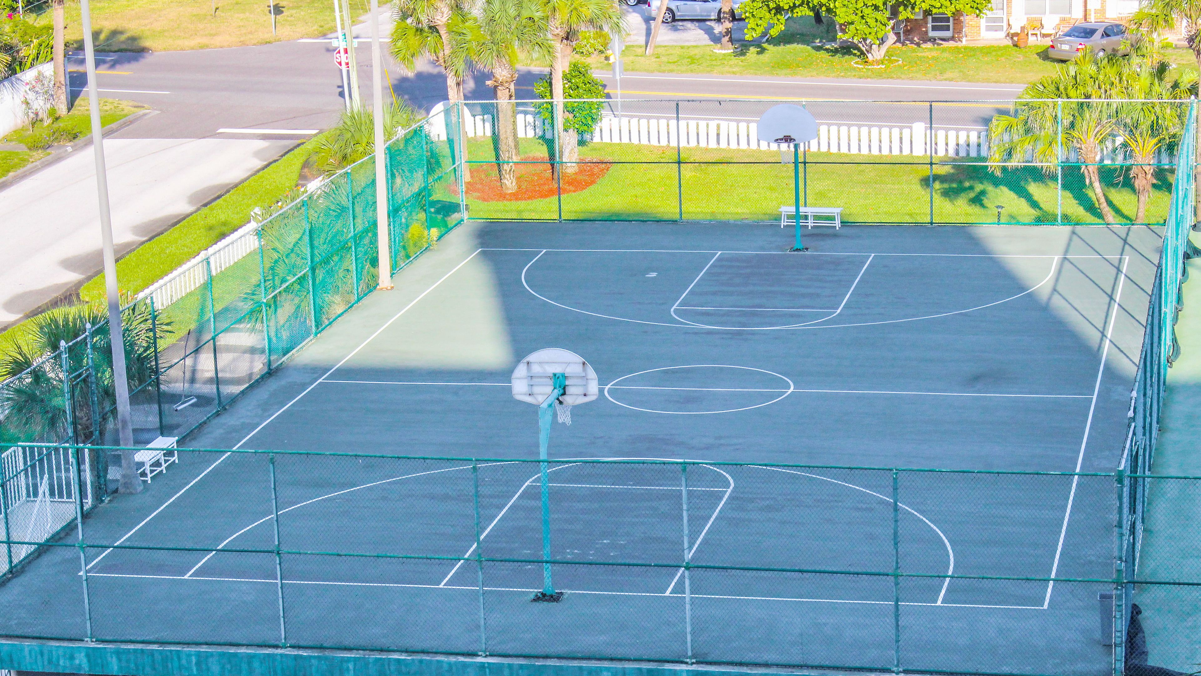 An outdoor basketball court with a green fence, a basketball hoop, and a bench.