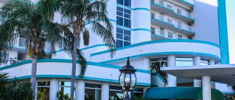 Um hotel com fachada curva, várias varandas e uma palmeira em primeiro plano.