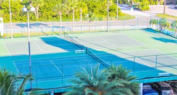 A tennis court with a net, surrounded by a fence and palm trees.