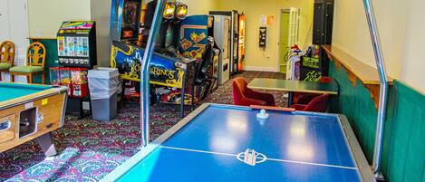 Una habitación con mesa de billar, juegos de arcade y dardos.