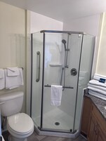 Un box de ducha con paredes y puerta de vidrio, un inodoro blanco y una pila de toallas blancas etiquetadas como 'POOL TOWELS' sobre una encimera.