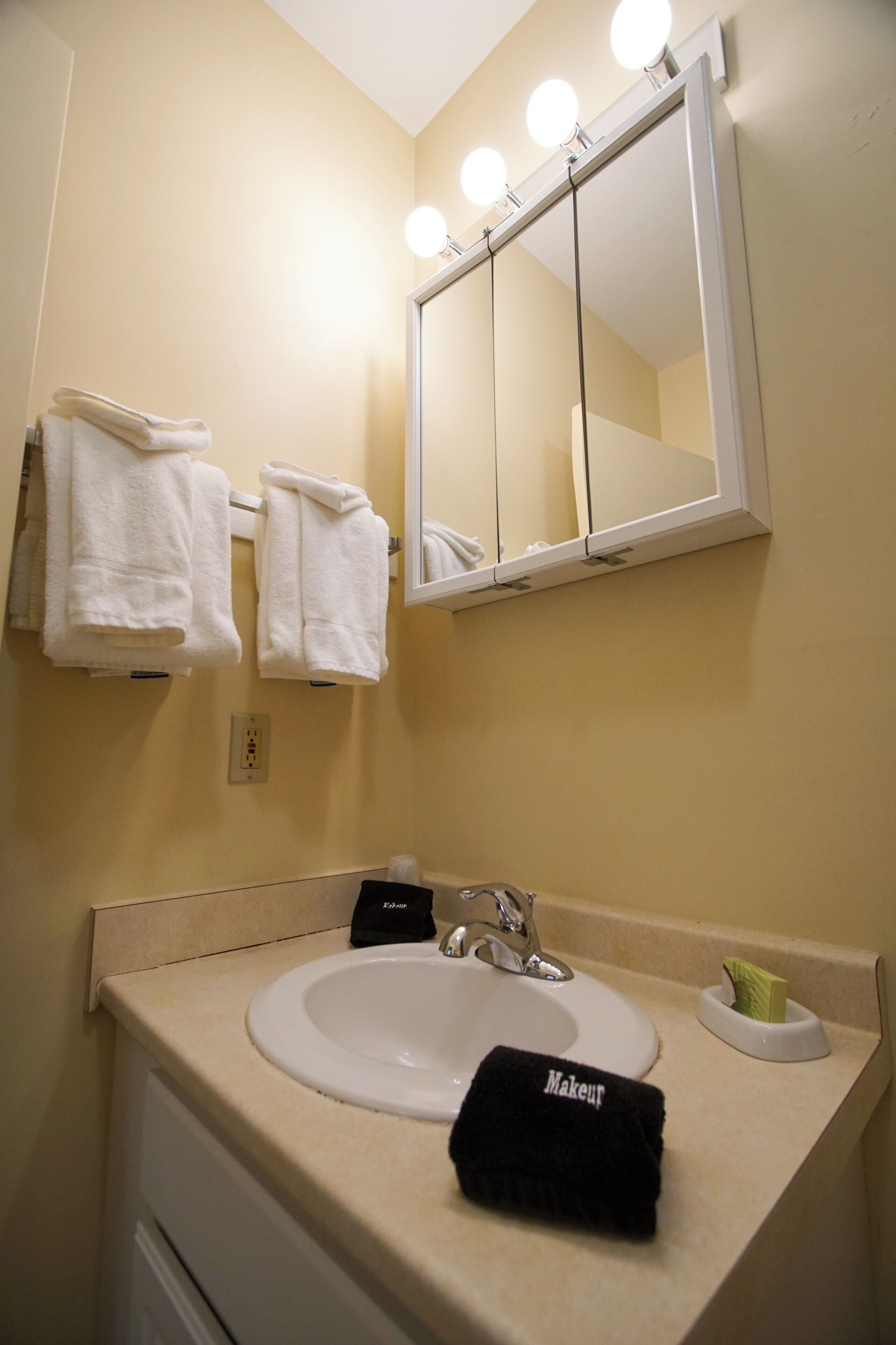A bathroom with a white sink, a mirror with lights, and towels on a rack.