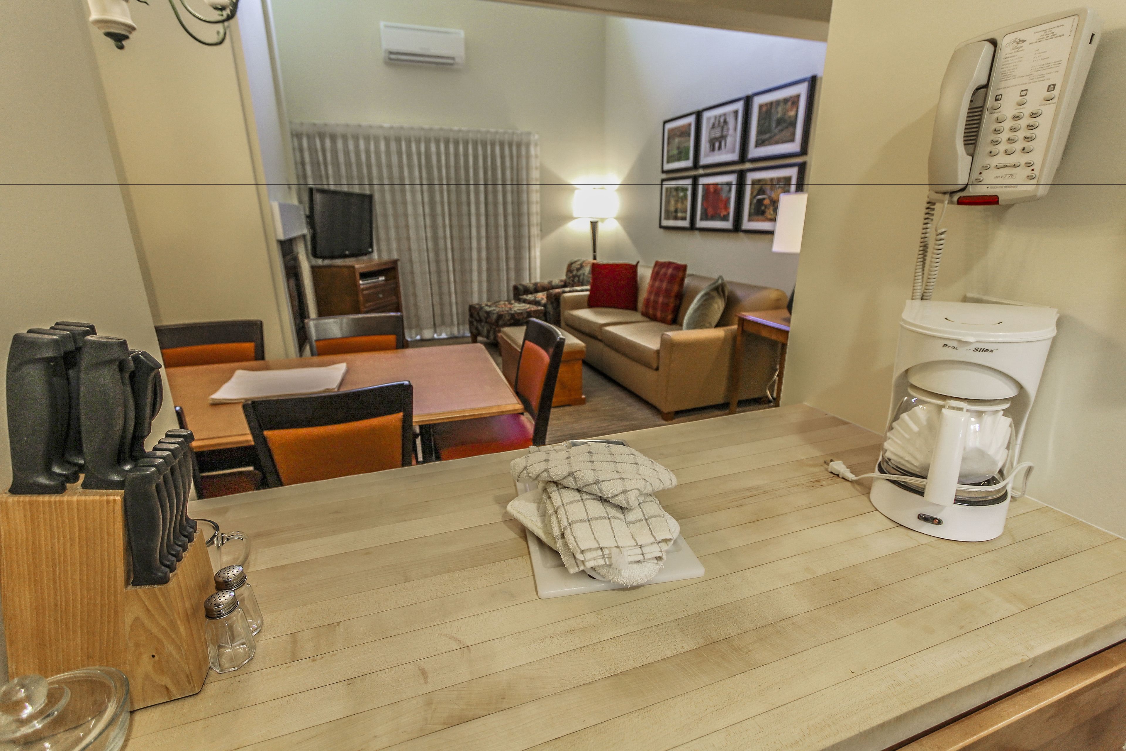 A hotel room with a wooden dining table, a coffee maker, a sofa, a TV, and a telephone.