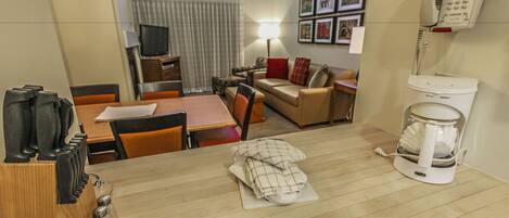 A hotel room with a wooden dining table, a coffee maker, a sofa, a TV, and a telephone.