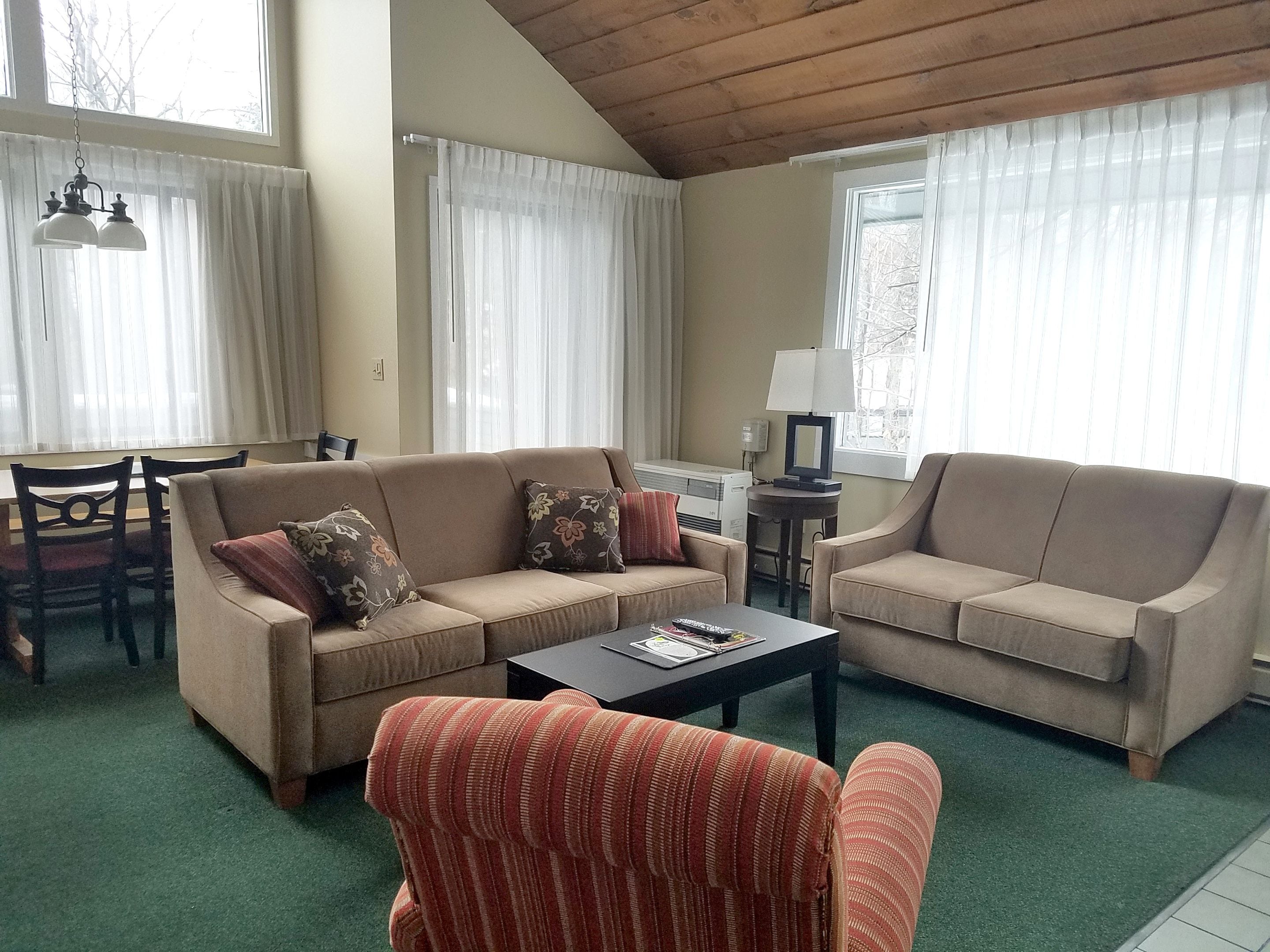 Una sala de estar con dos sofás, un sillón a rayas, una mesa de centro y un comedor con sillas y una mesa.