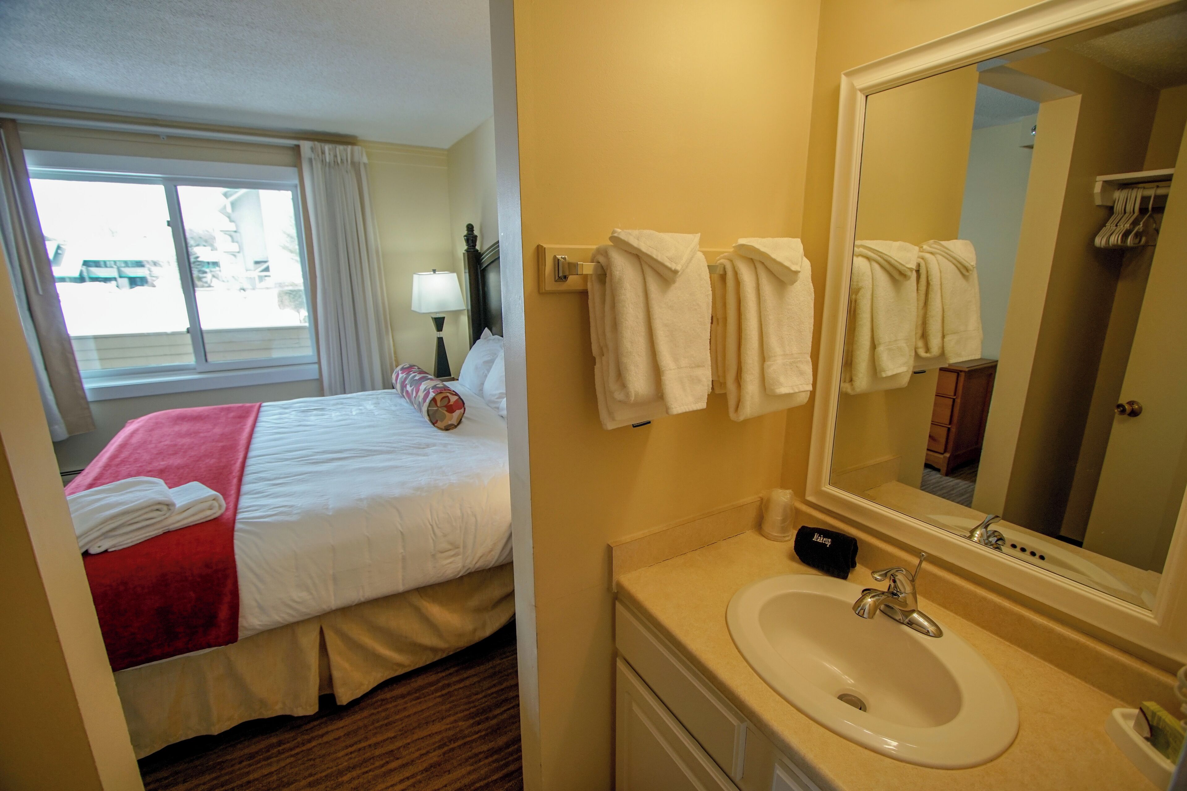 Une chambre d’hôtel avec un lit, une salle de bain comprenant un lavabo et un miroir, et des serviettes accrochées au mur.