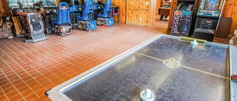 A room with a foosball table, arcade games, and a large pool table.