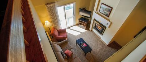 A high-ceilinged living room with a sofa, a coffee table, a TV, and a fireplace.