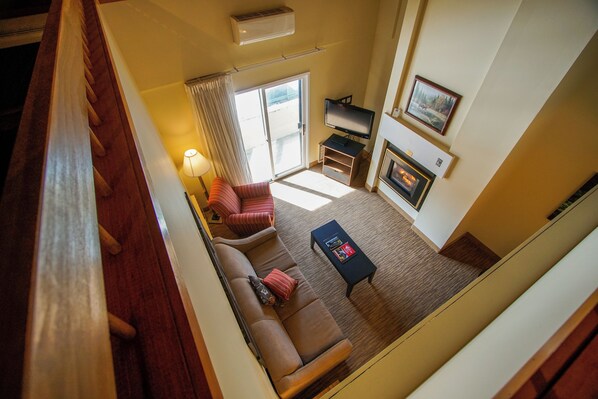 A high-ceilinged living room with a sofa, a coffee table, a TV, and a fireplace. - The Village of Loon Mountain (Lincoln)