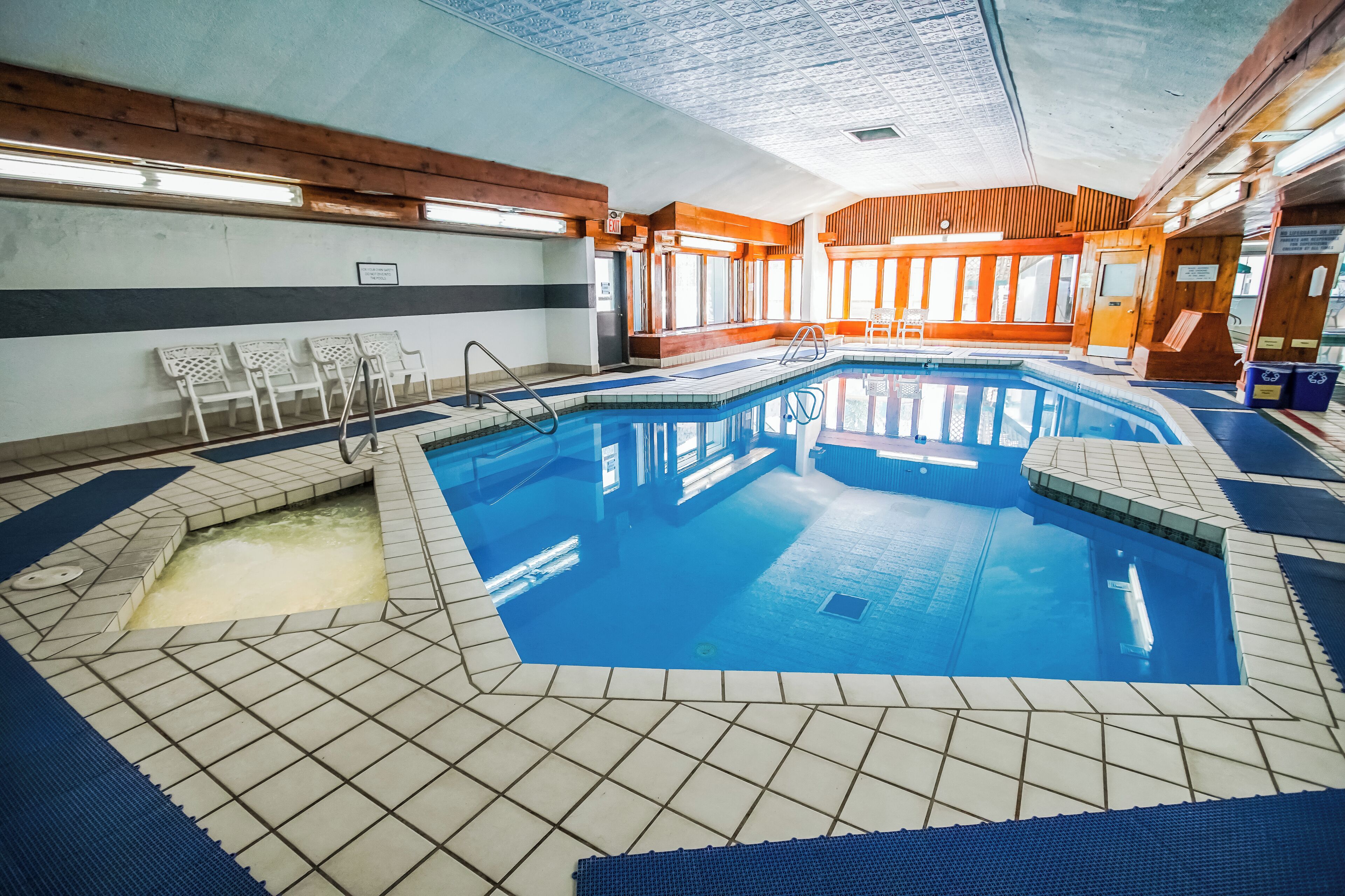 Una piscina interior amb sòl de rajola, parets de fusta i una zona de seients amb cadires.