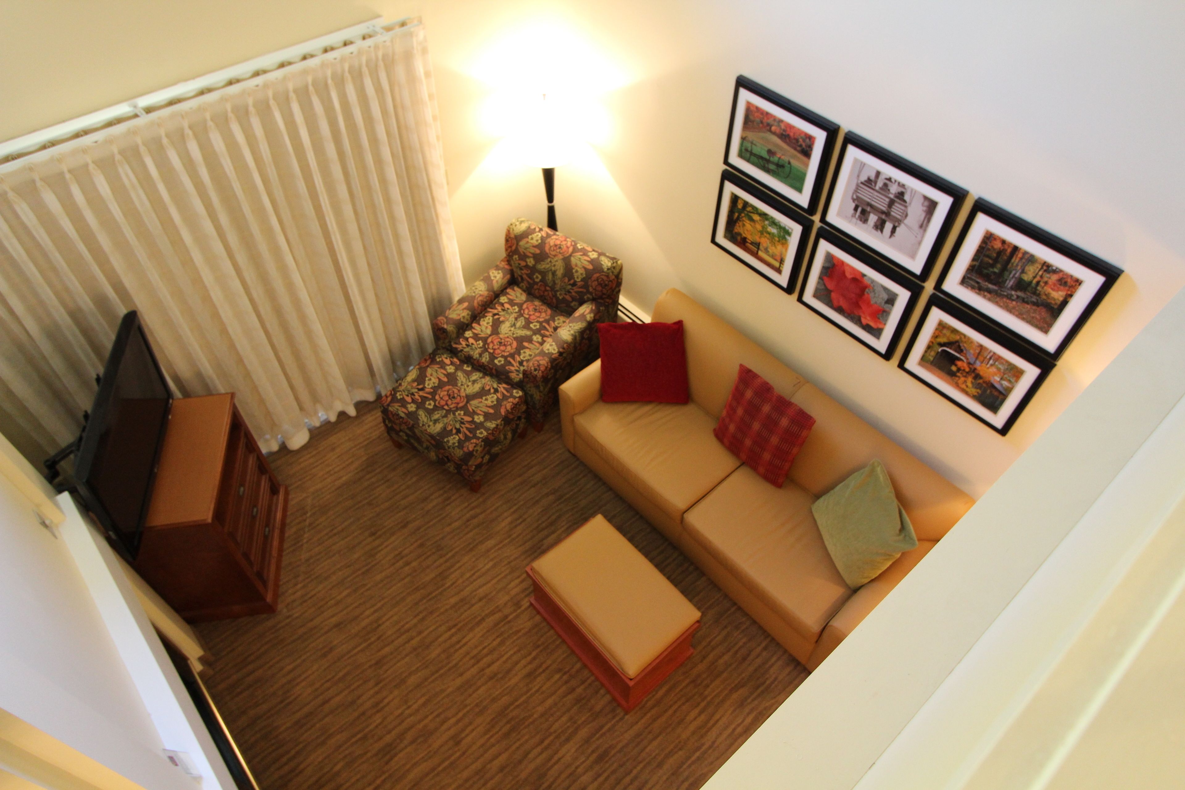 A living room with a sofa, a floral armchair, a small table, a lamp, and framed pictures on the wall.