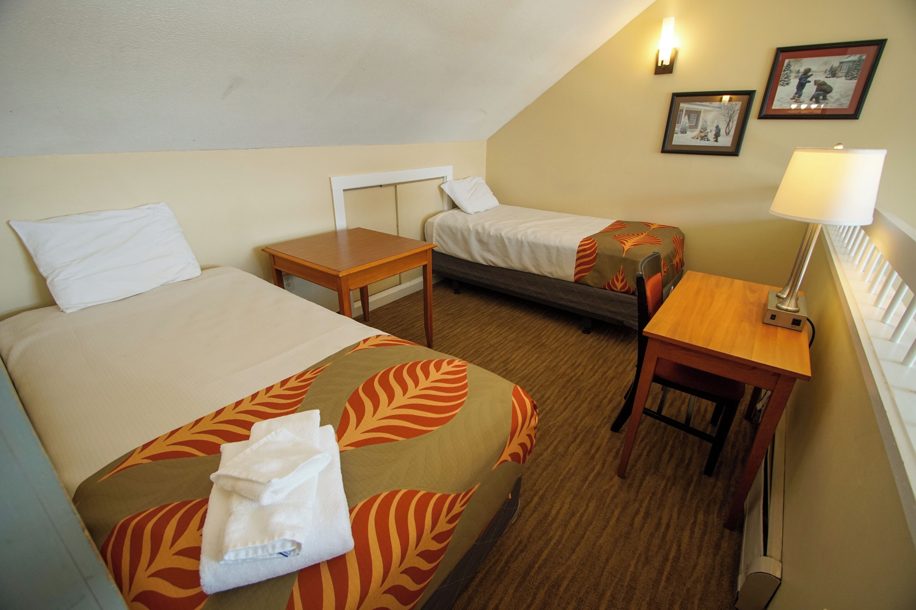 Habitación de hotel con dos camas, una mesita, una lámpara y un cuadro en la pared.