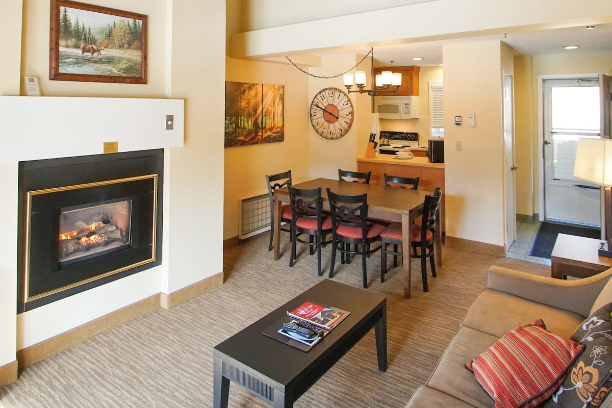 A spacious living room with a fireplace, a dining area, and a kitchen in the background.