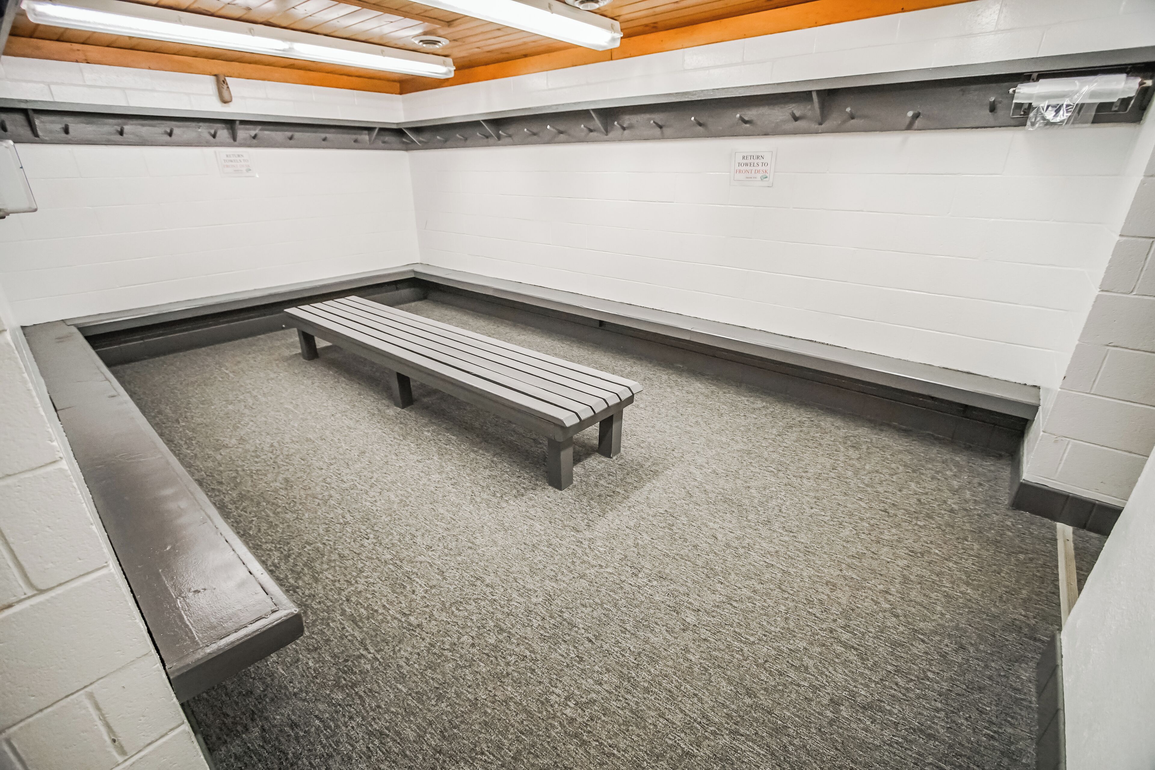 A restroom with two benches, white walls, and a wooden ceiling.