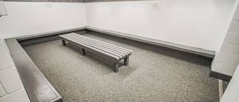 A restroom with two benches, white walls, and a wooden ceiling.